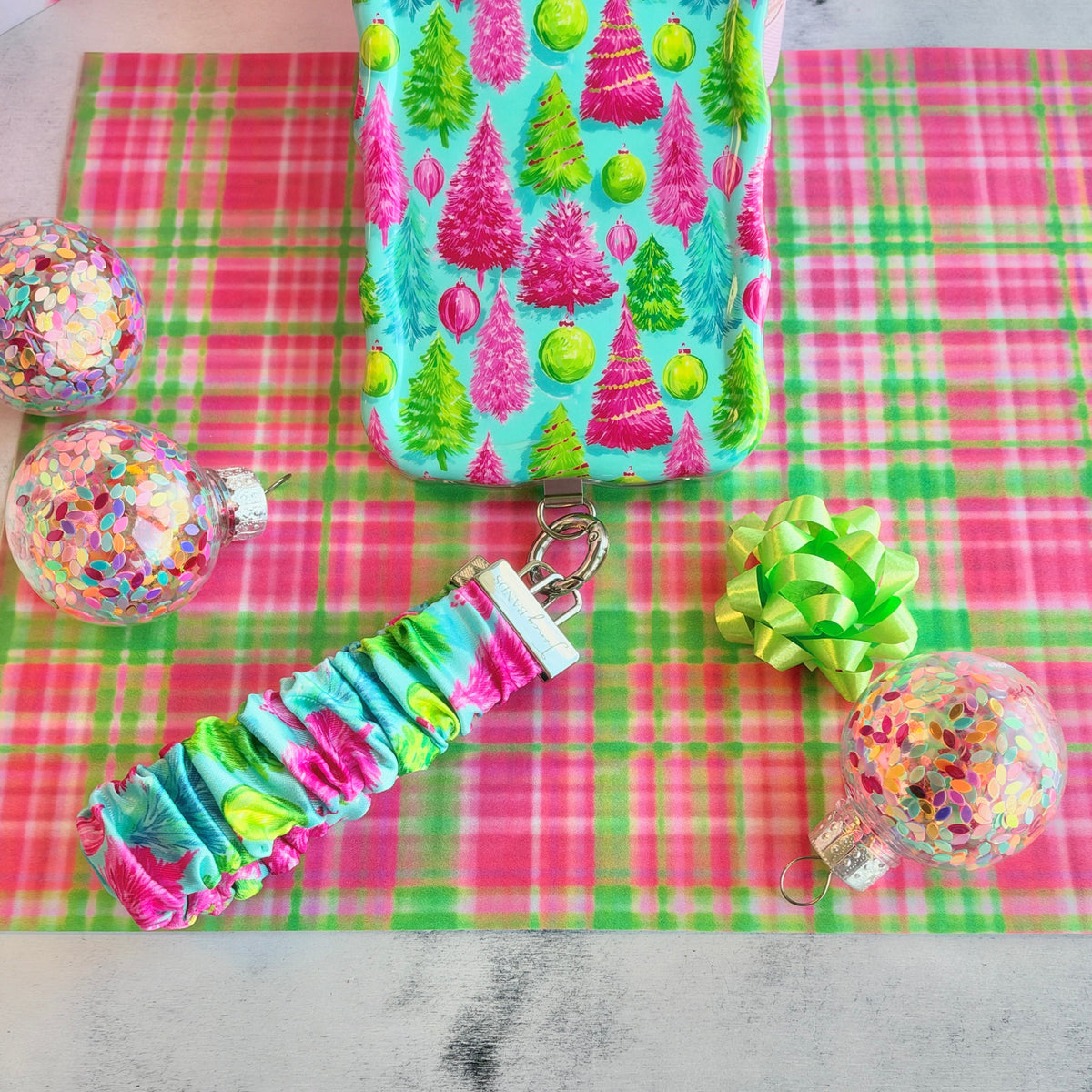 Merry & Bright, Totally! scrunchie phone wrist strap clipped below the matching Christmas tree iPhone case on pink and green plaid, with a lime bow and confetti ornaments