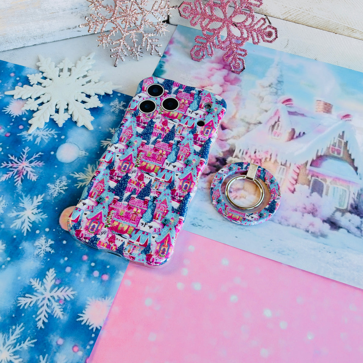 Sugarplum Square MagSafe grip ring lying beside the matching iPhone case on blue and pink snowflake paper