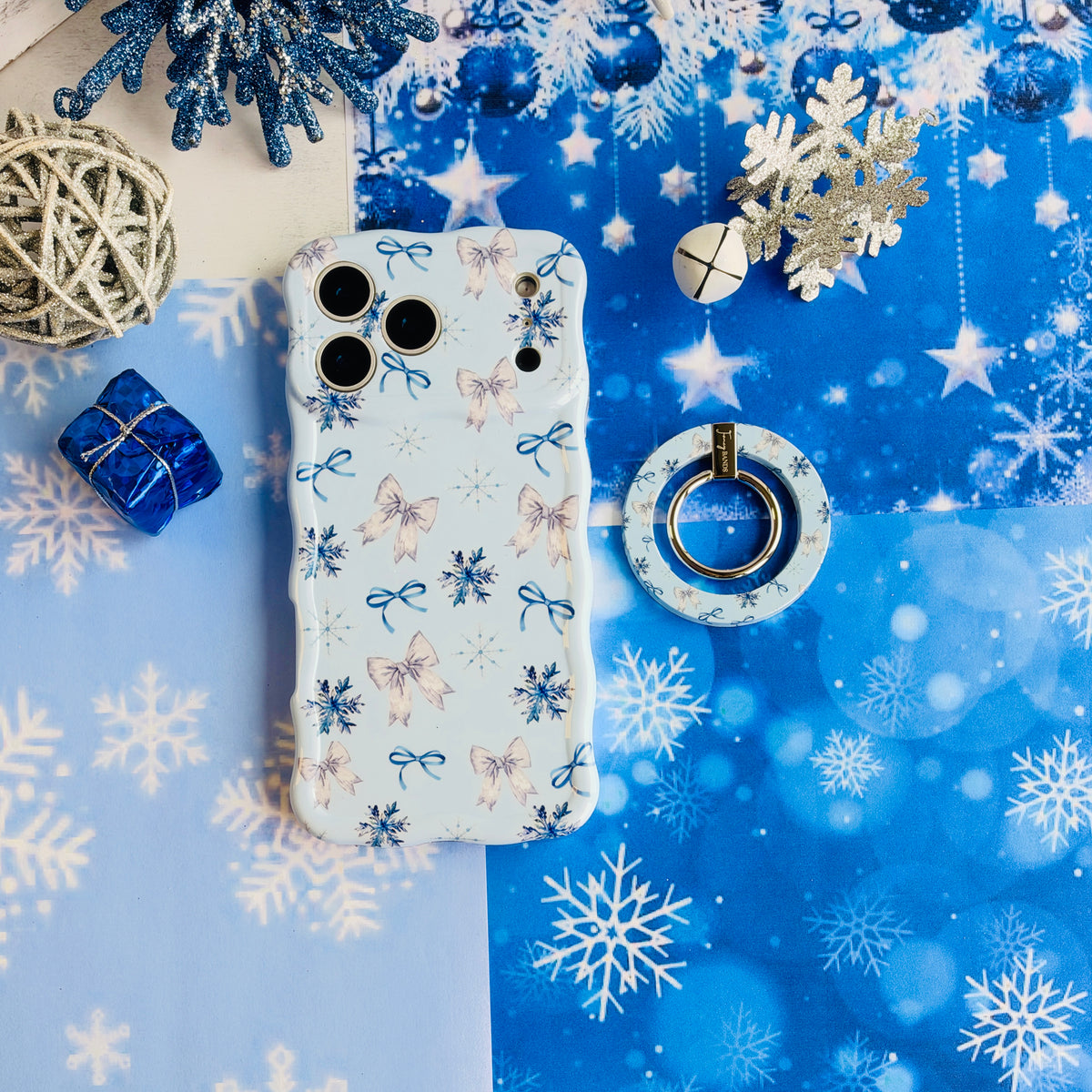 Snow Pretty In Blue MagSafe grip ring lying beside the matching iPhone case on blue snowflake paper with a blue gift box