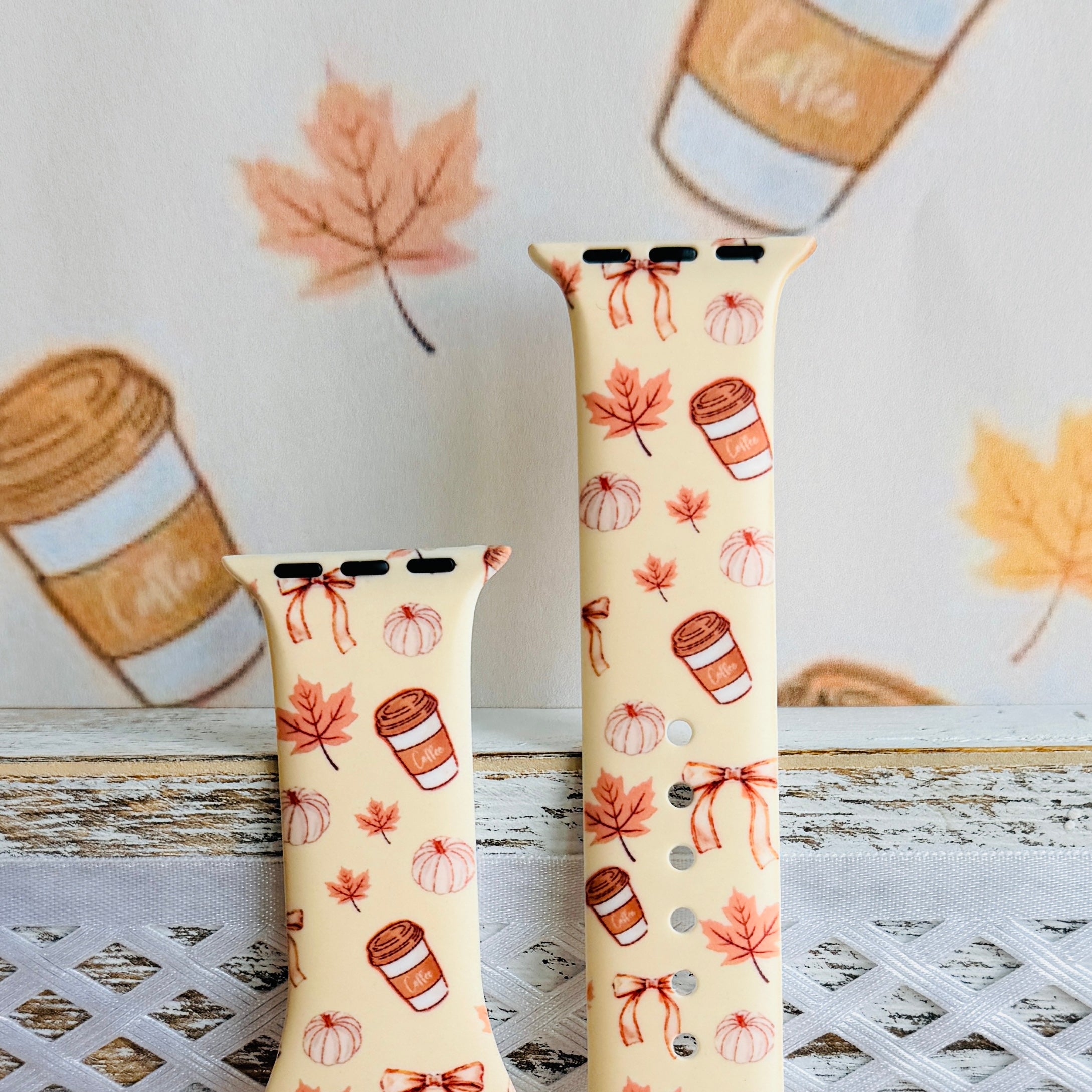 Both sizes of the Falling in Love a Latte Apple Watch band standing on a white bench, close view of the cream coffee cup and pumpkin print.