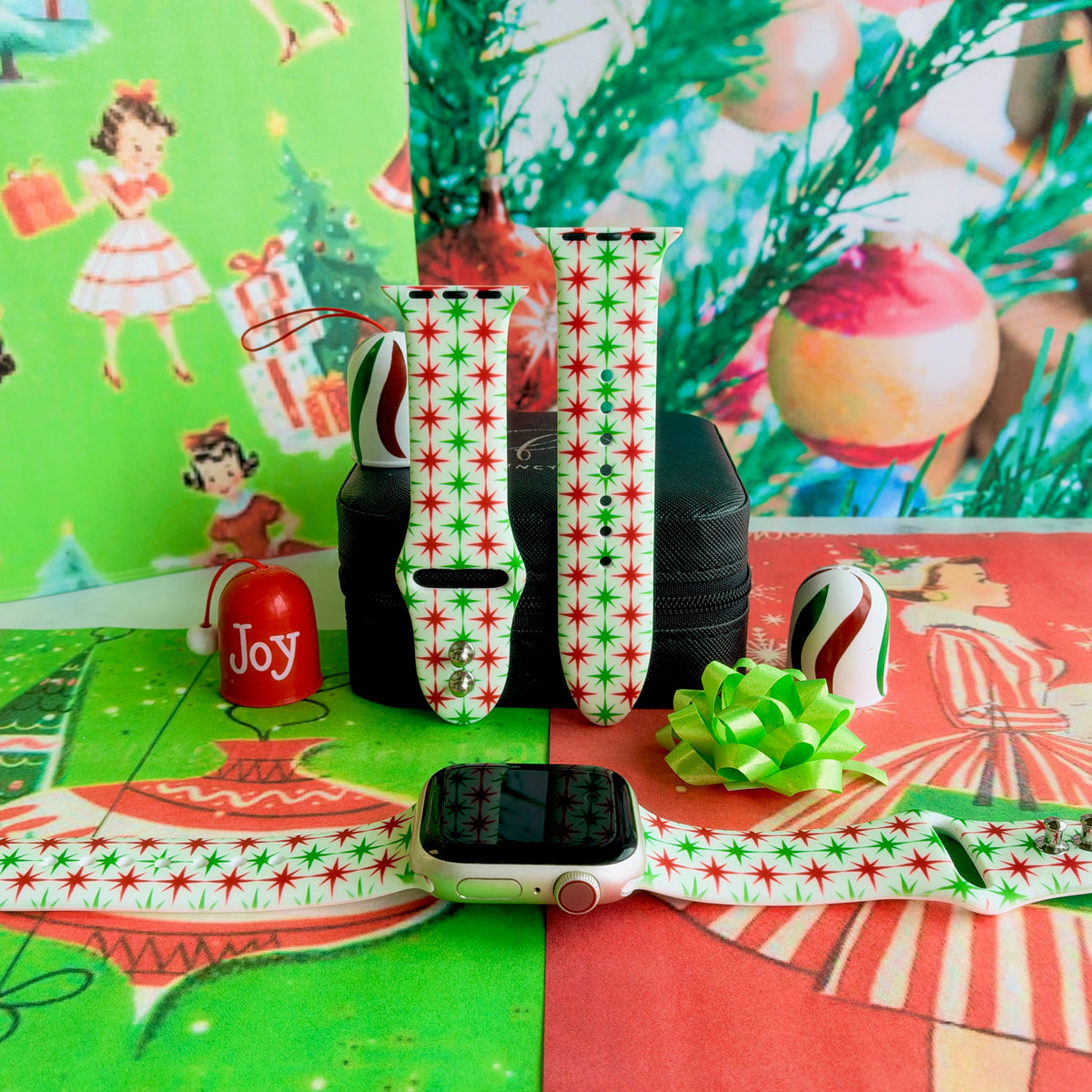 Tinsel & Stardust Apple Watch band on a rose gold Apple Watch and as two straps on a black jewelry box, red and green starbursts on cream