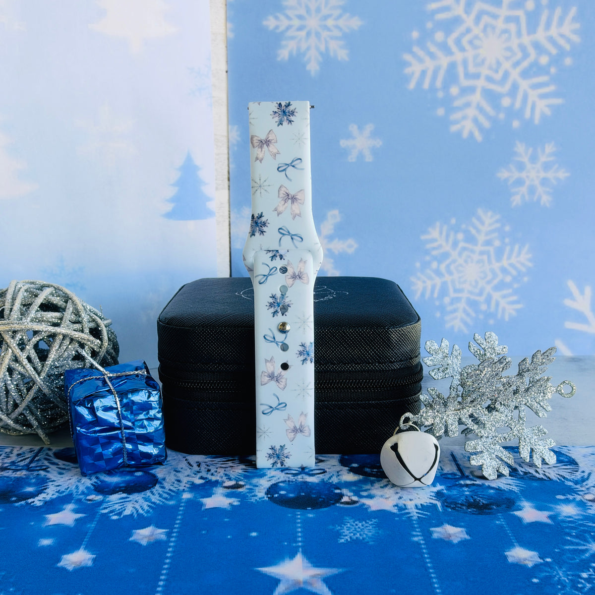 Single buckled Snow Pretty In Blue Samsung watch band strap standing on a jewelry box with a blue gift and a silver glitter snowflake