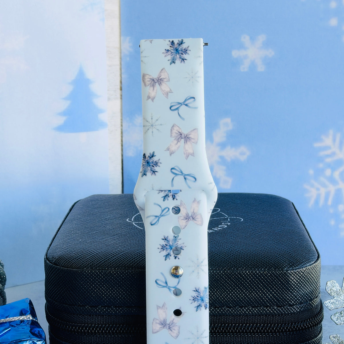 Close-up of a single Snow Pretty In Blue Samsung watch band strap, bow and snowflake print on pale icy blue