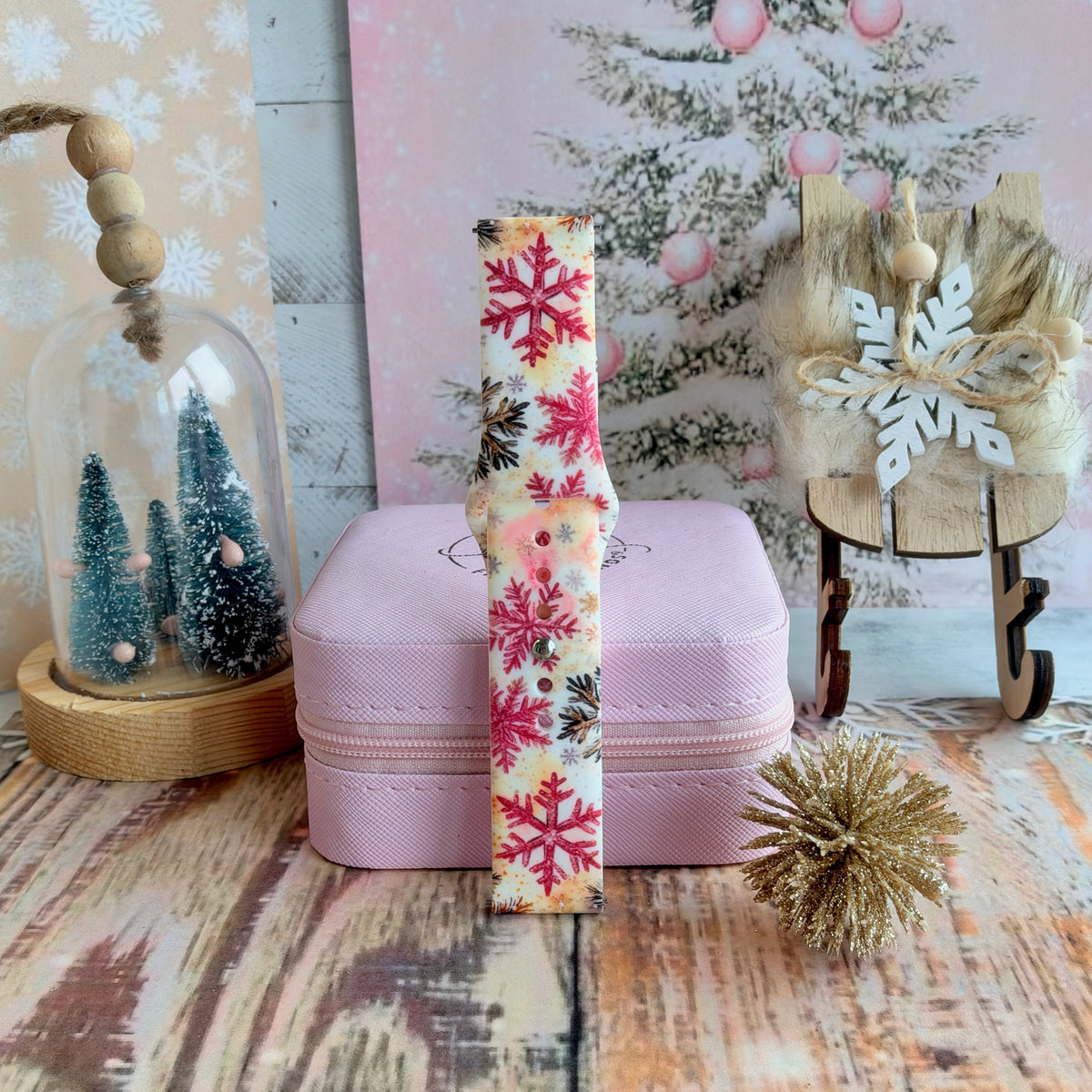 Single buckled Champagne Snowfall Samsung watch band strap standing on a pink jewelry box beside a wooden sleigh