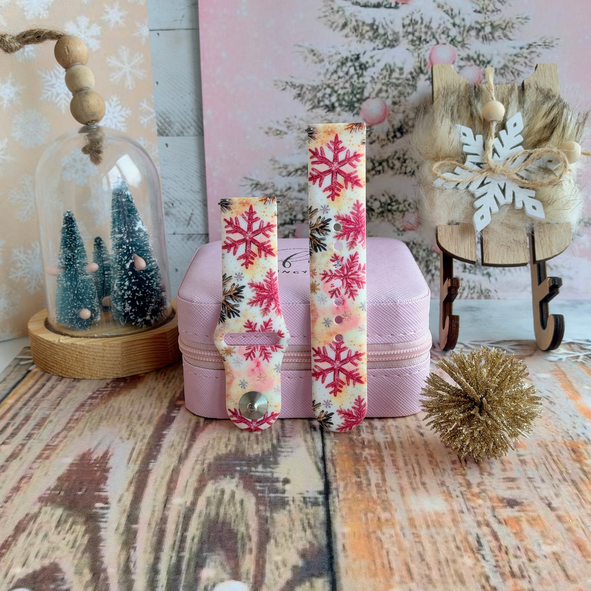 Both straps of the Champagne Snowfall Samsung Galaxy Watch band on a pink jewelry box with a gold glitter pom and bottle-brush trees