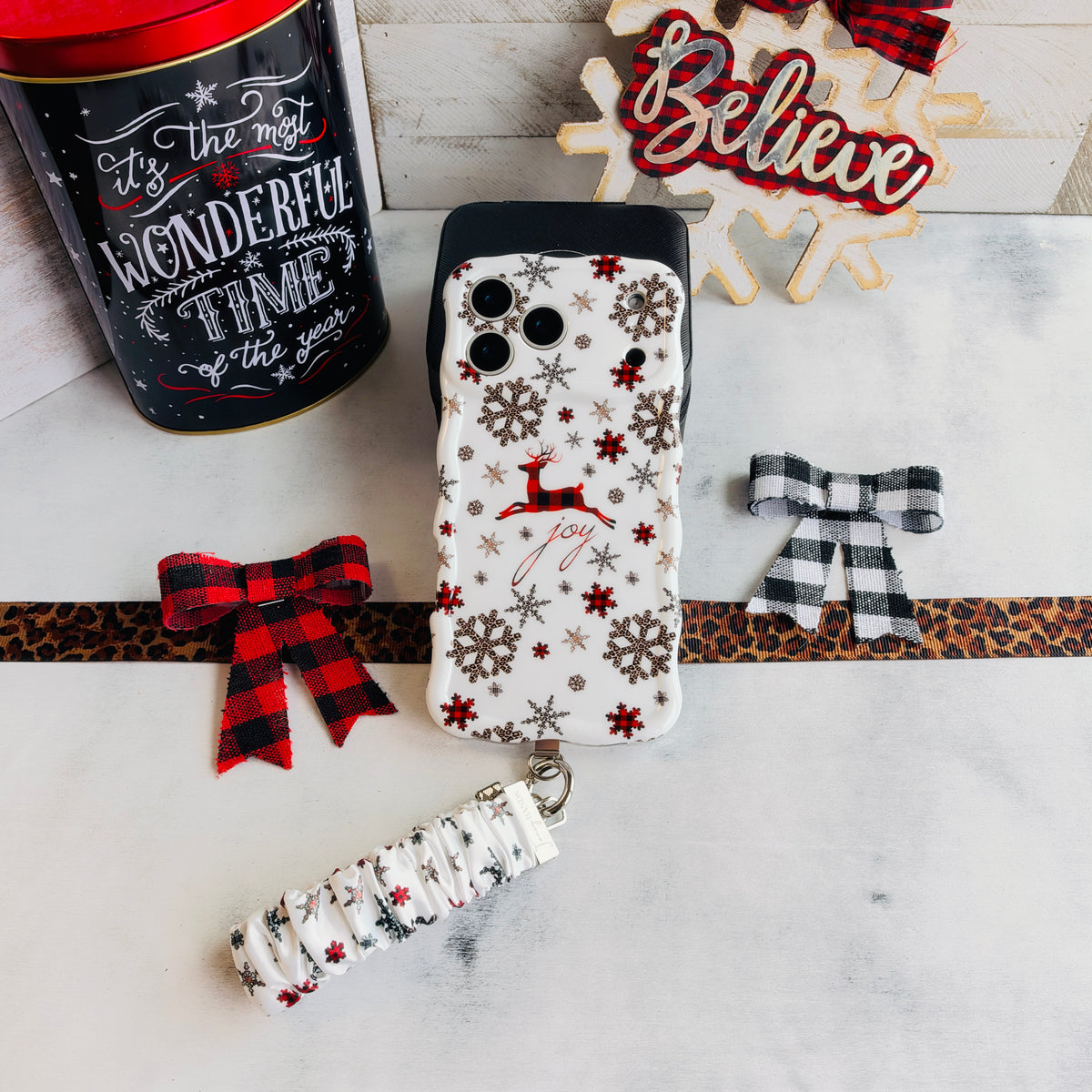Deer Joy iPhone case with its white snowflake scrunchie wrist strap beside a Most Wonderful Time of the Year tin and a Believe sign