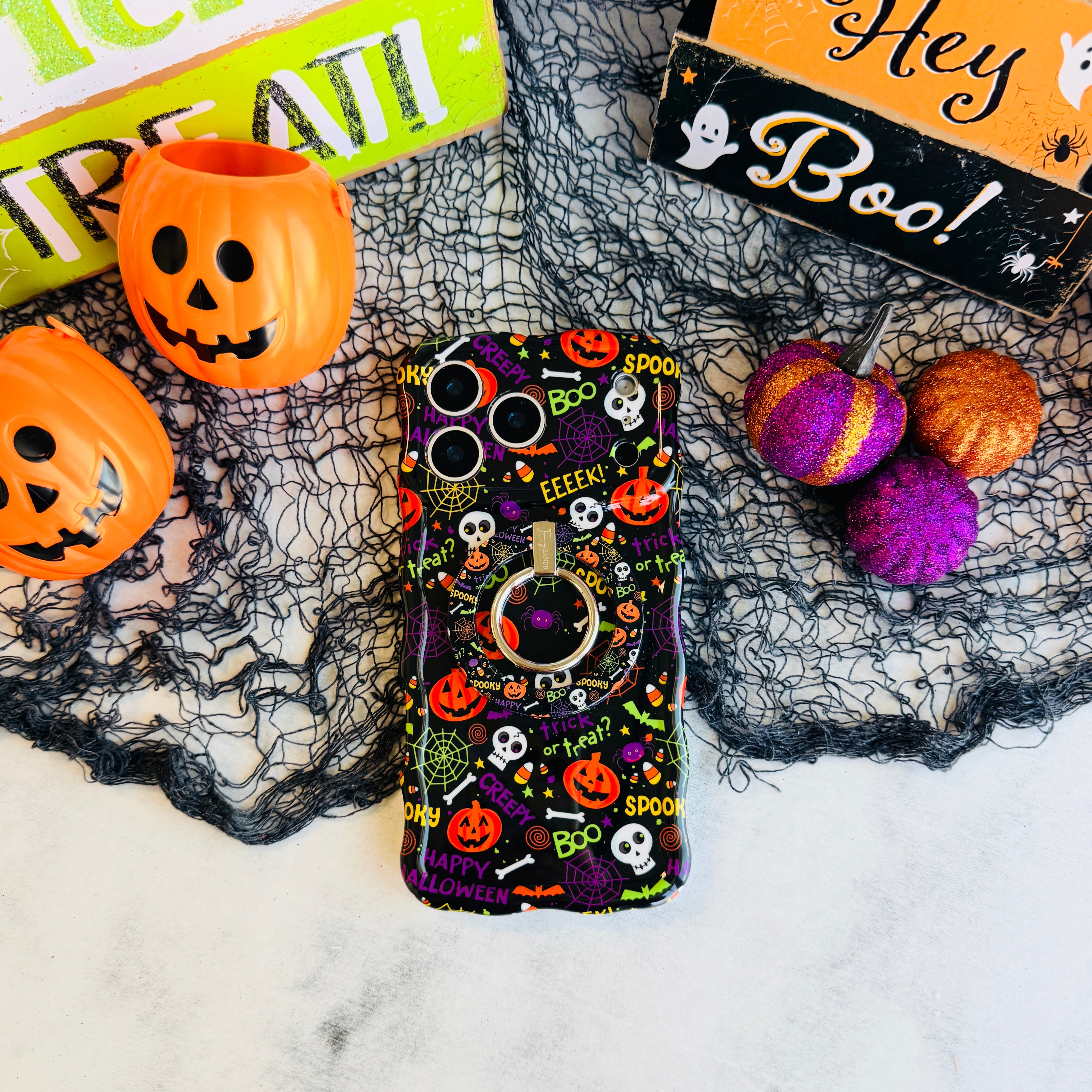 Spooky Hold It Fancy MagSafe grip ring attached to the matching Wavy Luxe iPhone case, styled with orange pails and purple felt pumpkins