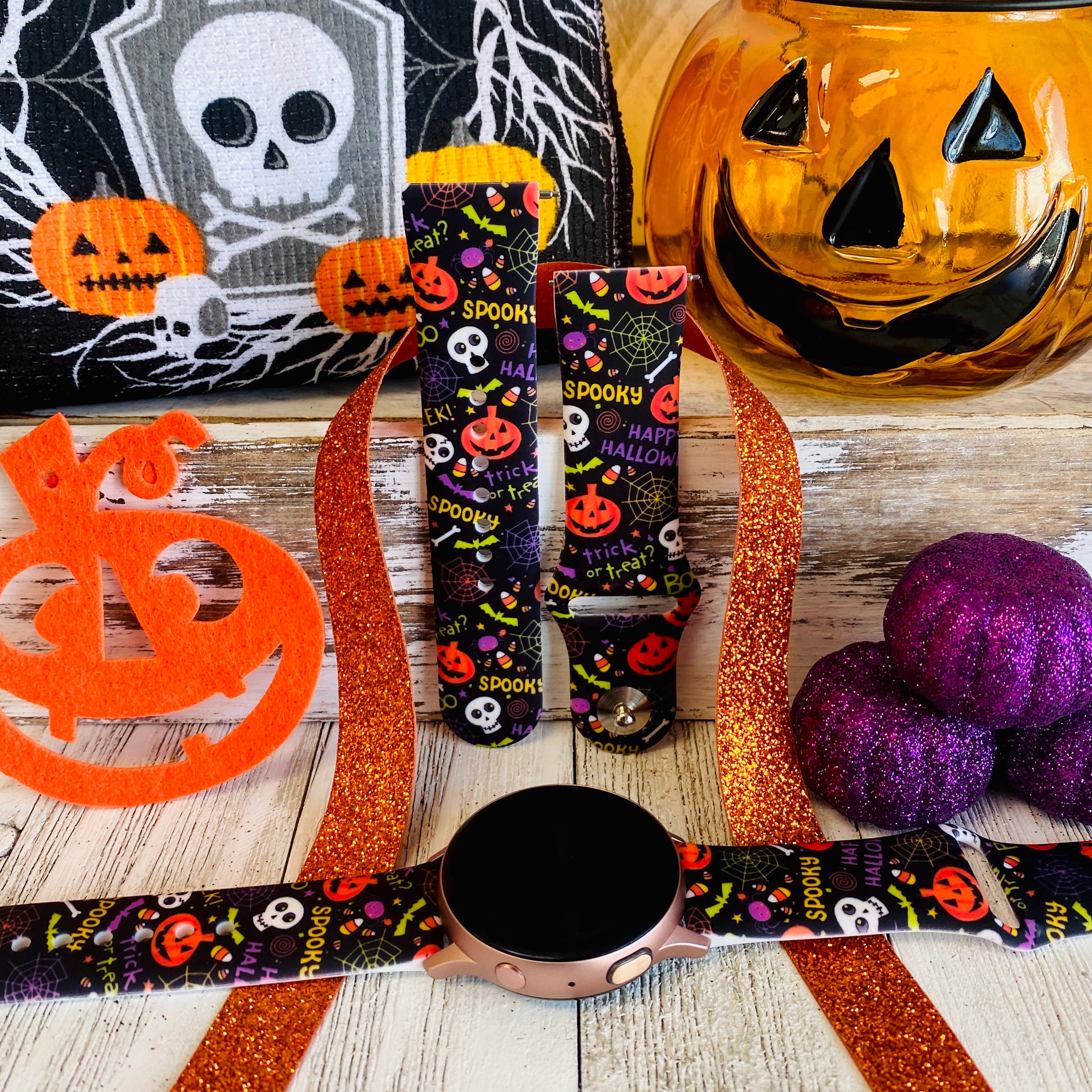 Spooky silicone Samsung Galaxy Watch band hero shot in black with orange pumpkins and skulls, shown with a rose gold Galaxy Watch.