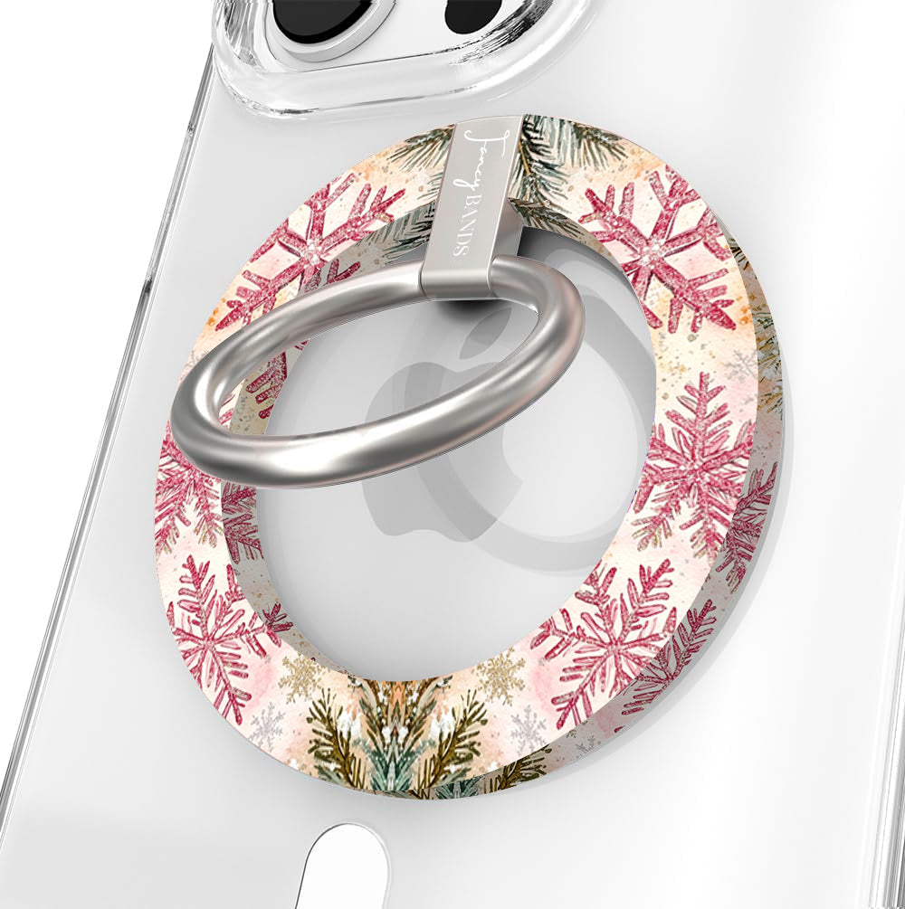 Close-up of the Champagne Snowfall MagSafe grip ring with pink and gold glitter snowflakes and a brushed silver ring on a clear iPhone case