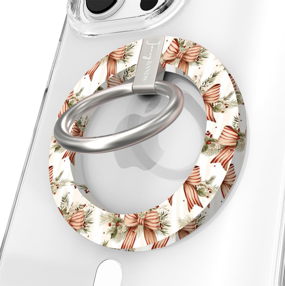 Close-up of the Deck Yourself in Bows & Holly MagSafe grip ring with red ribbon bows and pine on ivory and a brushed silver ring on a clear iPhone case