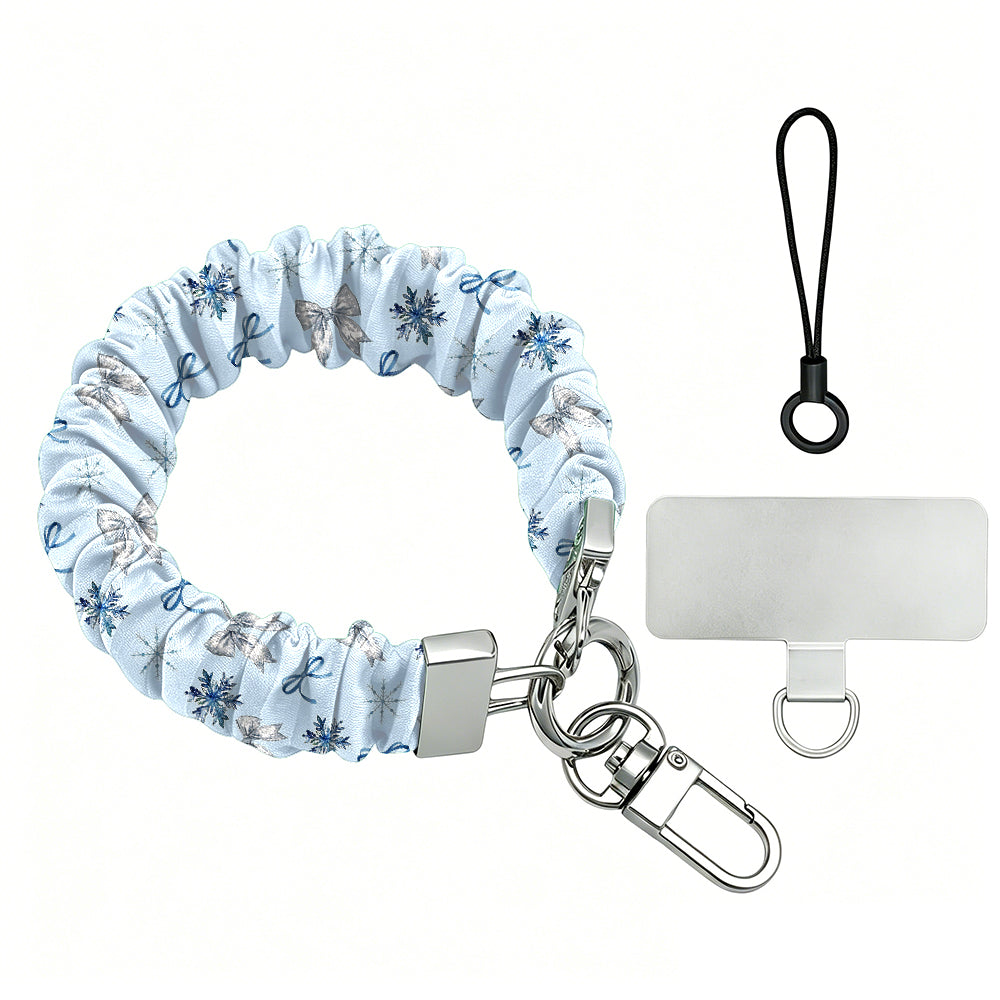 Snow Pretty In Blue scrunchie phone wrist strap laid flat with silver clasp and phone tab, silver bows and navy snowflakes on powder blue