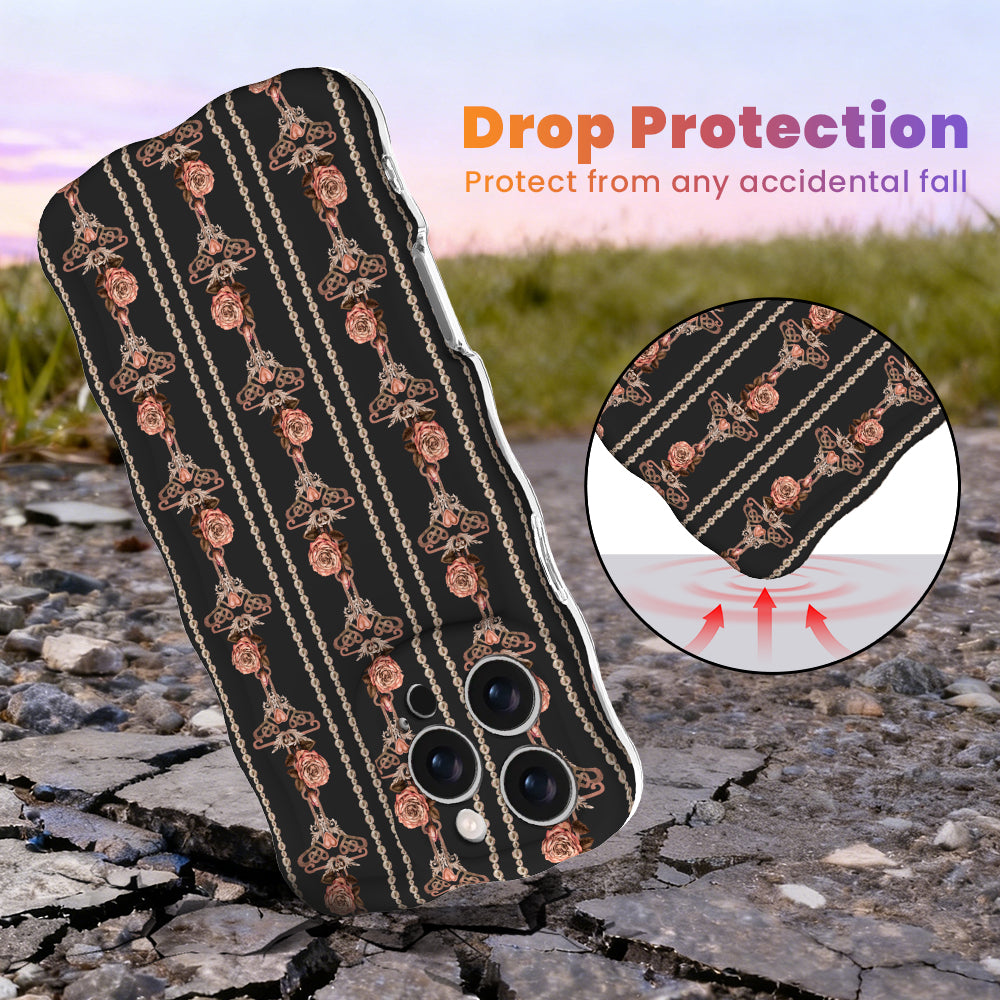 Pretty Little Details black Wavy Luxe MagSafe iPhone case with champagne pearl strands and rose gold rose drops, standing on cracked rock at sunset with an inset of the cushioned drop-protection edge.