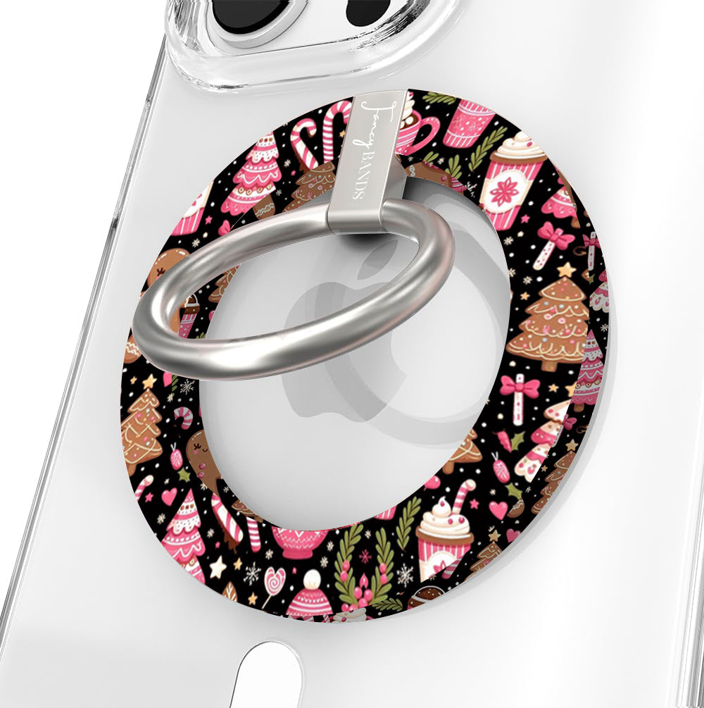 Close-up of the Merry Mugs & Ginger Hugs MagSafe grip ring, black gingerbread print with pink cocoa mugs and candy canes, with brushed silver ring on a clear iPhone case