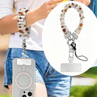 Fall Floral Bliss scrunchie phone wrist strap worn on the wrist with a phone in a clear MagSafe case, with an inset close-up of the cream floral strap, silver clasp, and attachment tab.