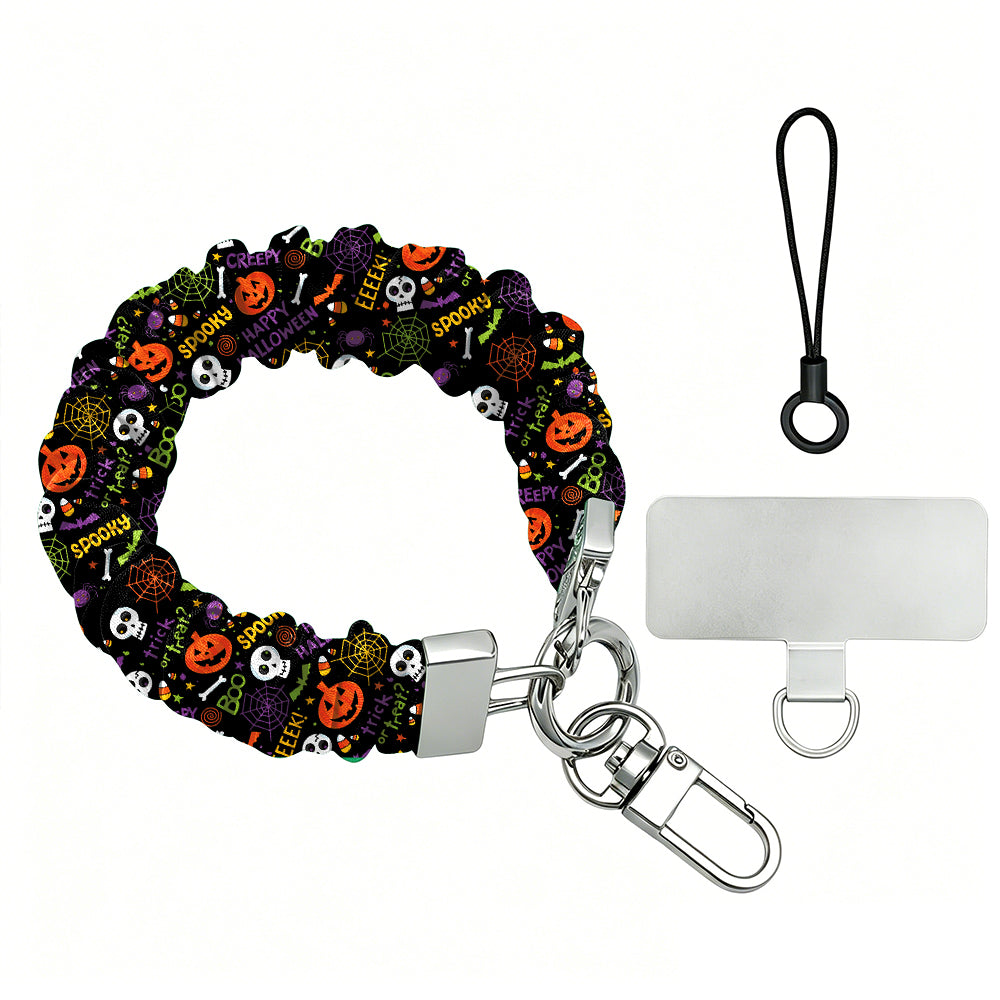 Spooky scrunchie phone wrist strap shown with its metal clasp and phone attachment tab, black fabric printed with pumpkins, skulls and spiderwebs.