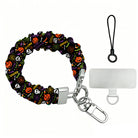Spooky scrunchie phone wrist strap shown with its metal clasp and phone attachment tab, black fabric printed with pumpkins, skulls and spiderwebs.