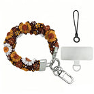 Harvest Sunflowers scrunchie phone wrist strap on a white background, showing the deep brown fabric packed with golden sunflowers and white daisies, silver lobster clasp, black loop cord, and clear attachment tab.