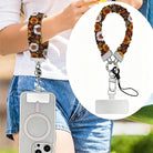 Harvest Sunflowers scrunchie phone wrist strap worn on the wrist with a phone in a clear MagSafe case, with an inset close-up of the brown sunflower strap, silver clasp, and attachment tab.