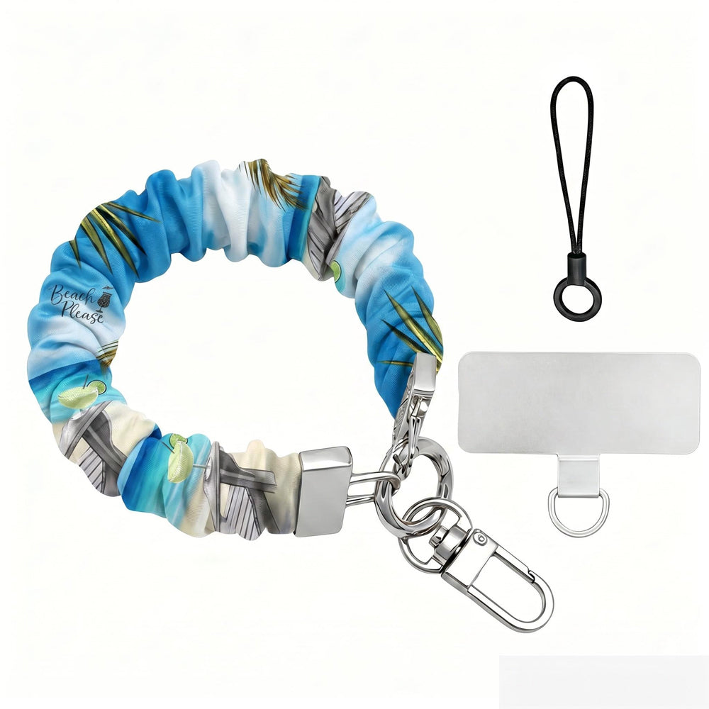 Blue and green satin Beach Please scrunchie phone wrist strap clipped to the matching Beach Please Wavy Luxe iPhone case with a beach chair and cocktail design, styled on a sandy shoreline background with starfish and ocean waves.