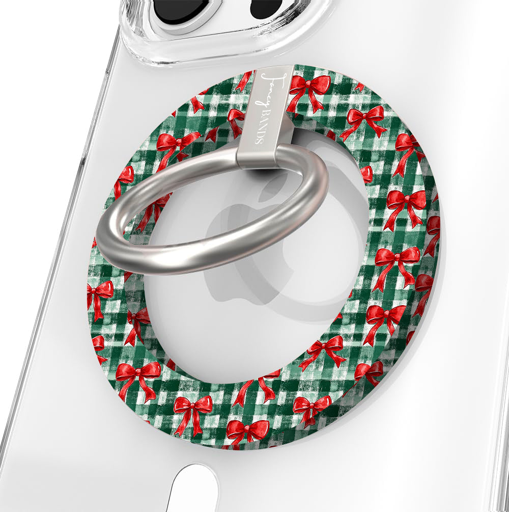 Close-up of the Plaid Tidings & Bows MagSafe grip ring with red bows on green gingham and a brushed silver ring on a clear iPhone case