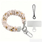 A sweet Bee Happy scrunchie phone wrist strap in a white bumblebee, honeycomb, and honey-pot print, clipped to the matching Bee Happy Wavy Luxe iPhone case, styled with sunflowers and bees on a soft cream background.
