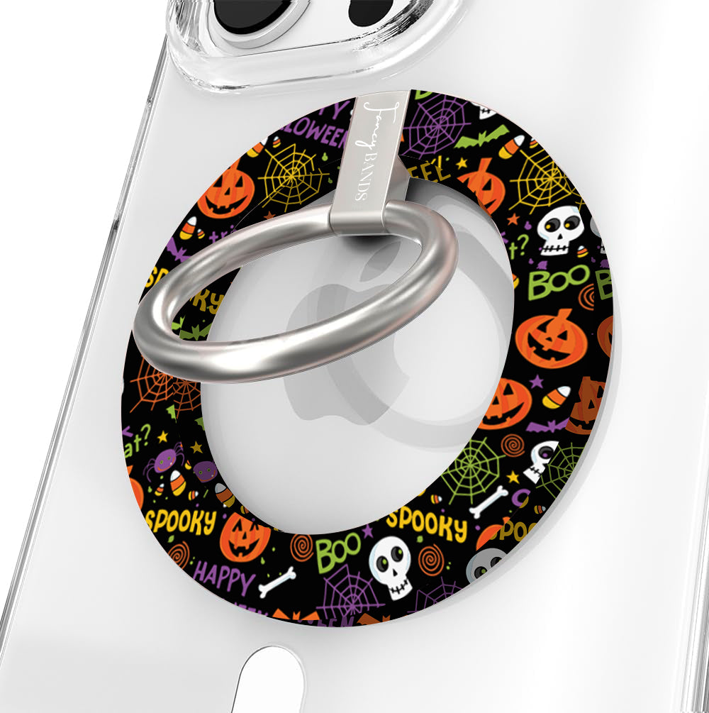 Spooky Hold It Fancy MagSafe grip ring shown on a clear iPhone case, black ring covered in orange pumpkins, white skulls and spiderwebs.