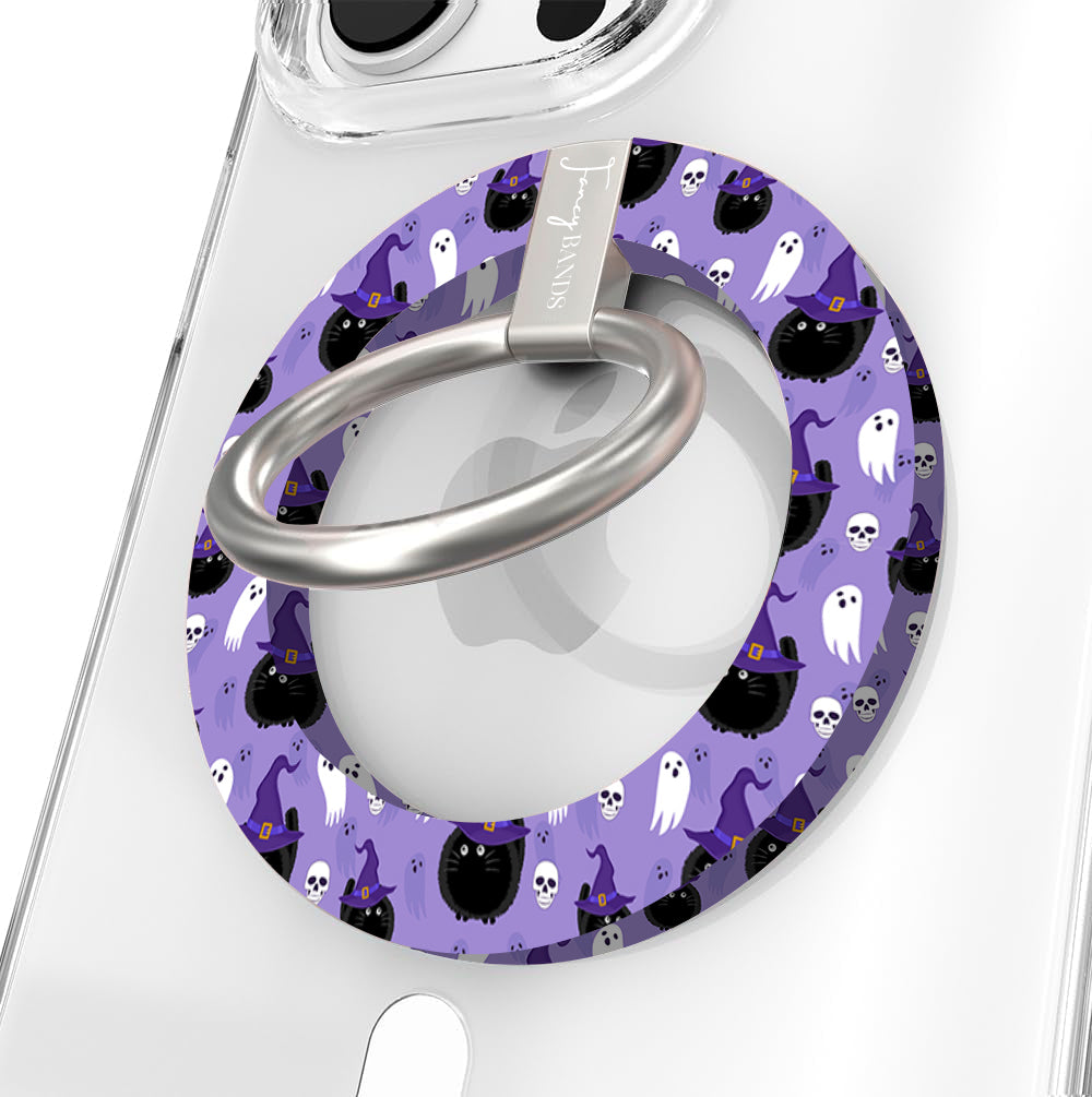 Ghostly Whisker's Hold It Fancy MagSafe grip ring close-up on a clear iPhone case, showing the lavender ring with white ghosts, black cats and witch hats around the silver rotating ring.