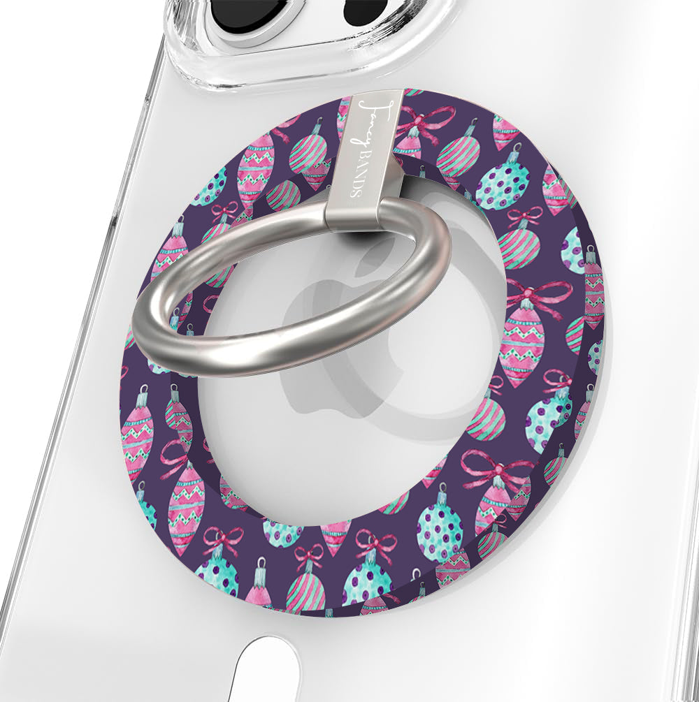 Close-up of the Just One More Ornament MagSafe grip ring with pink and aqua ornaments on plum and a brushed silver ring on a clear iPhone case
