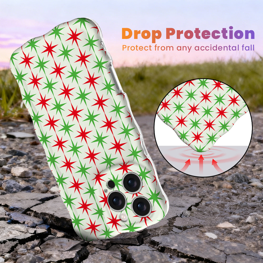 Tinsel & Stardust Wavy Luxe MagSafe iPhone case, red and green starbursts on cream, standing on cracked pavement to show drop protection