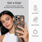 Get a Grip infographic for the Haunted Blossoms MagSafe grip ring, showing a model holding her black and orange gothic floral phone one-handed plus easy selfies, added comfort, and video stand uses.