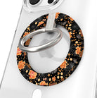 Haunted Blossoms Hold It Fancy MagSafe grip ring close-up on a clear iPhone case, showing the black ring with burnt-orange roses, mushrooms and gold spiderwebs around the silver rotating ring.