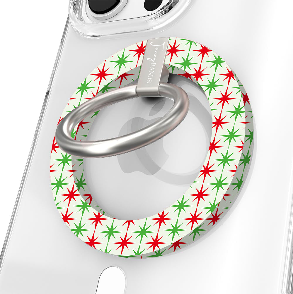 Close-up of the Tinsel & Stardust MagSafe grip ring with red and green starbursts on cream and a brushed silver ring on a clear iPhone case