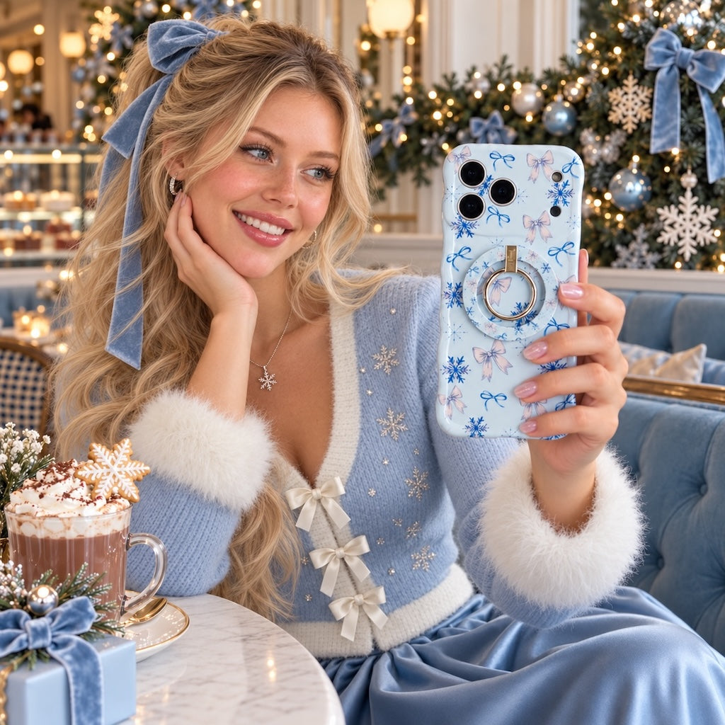 Woman in a blue cardigan with white fur cuffs holding the Snow Pretty In Blue iPhone case with matching grip ring in a café with hot cocoa