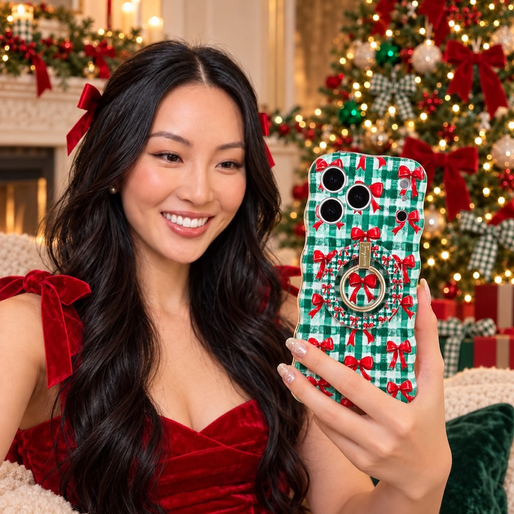 Woman in a red velvet top with a red hair bow taking a mirror selfie with the Plaid Tidings & Bows iPhone case and matching grip ring