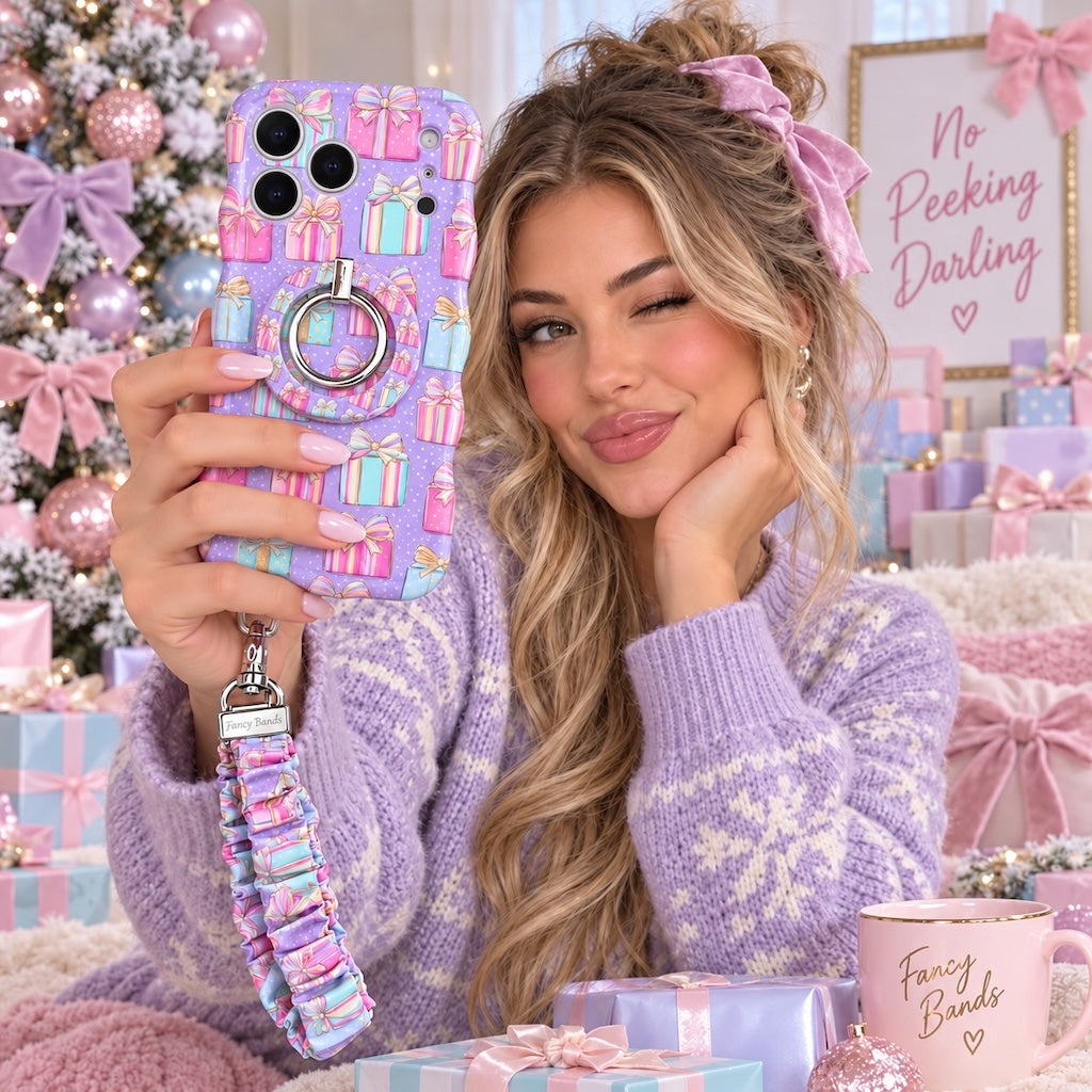 Woman winking while holding the No Peeking, Darling iPhone case with matching grip ring and scrunchie wrist strap in a pastel Christmas room
