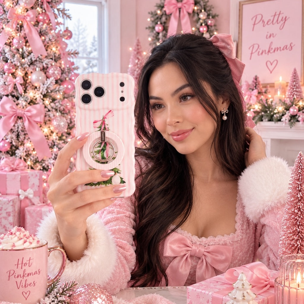 Woman in a pink fur-trimmed robe with a Hot Pinkmas Vibes mug, taking a selfie with her Pretty in PinkMas iPhone case and matching grip ring by pink Christmas trees