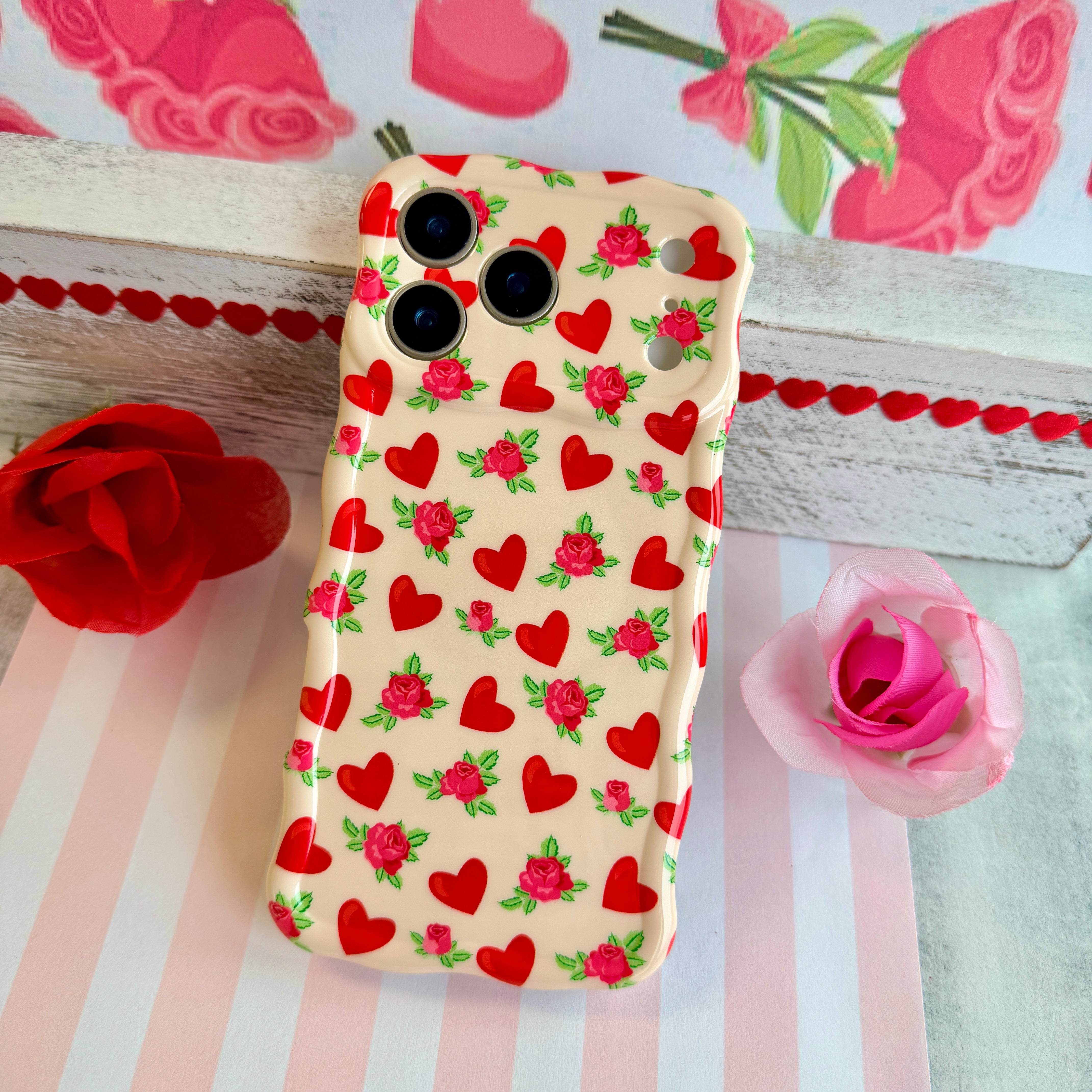 Cream colored wavy iPhone case featuring a pattern of red hearts and small pink roses with green leaves.