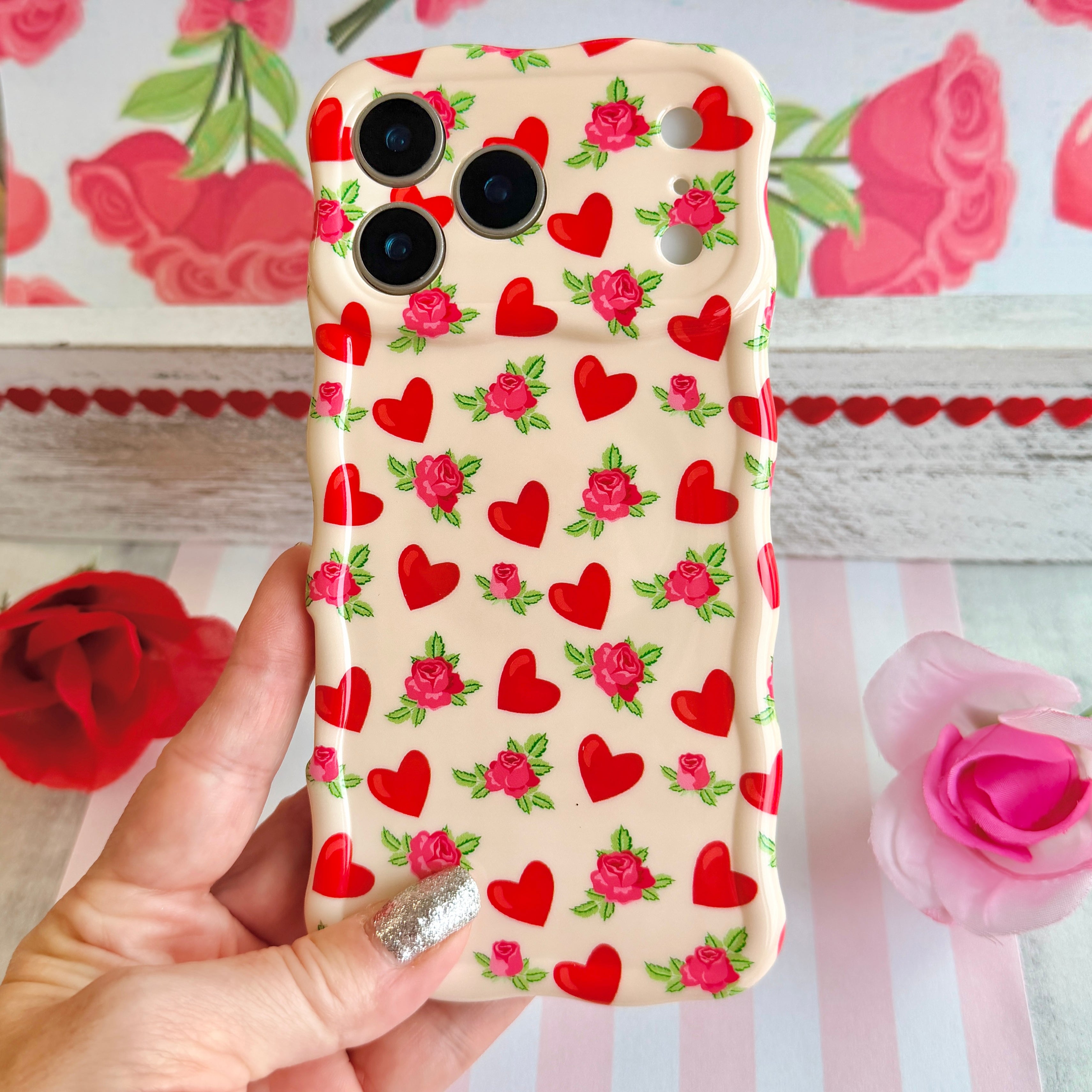 Cream colored wavy iPhone case featuring a pattern of red hearts and small pink roses with green leaves.