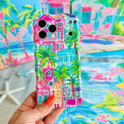 Hand holding the La Palma Villa Wavy Luxe MagSafe iPhone case, painted pink villas and palm trees on a tropical backdrop