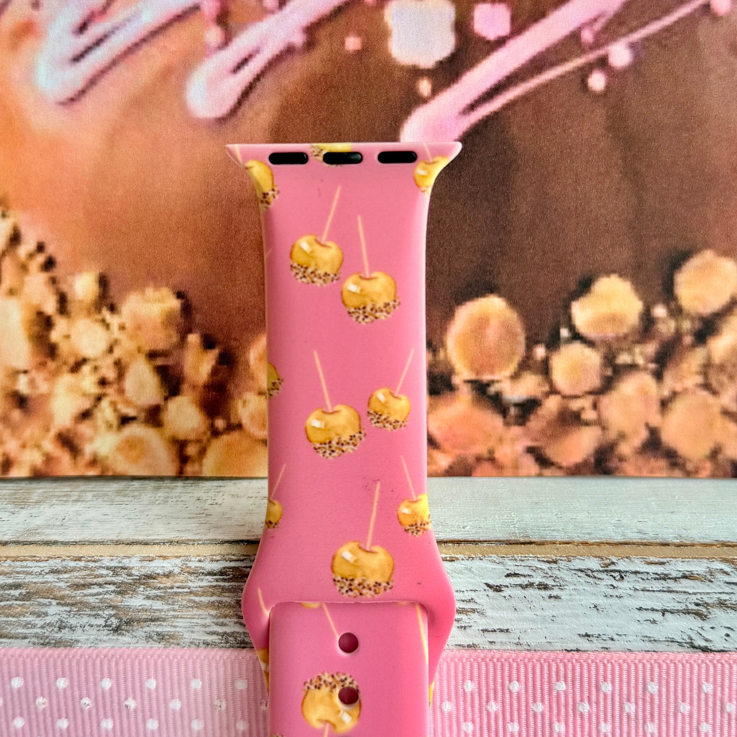 Close-up of the Caramel Coated Cutie Apple Watch band showing the glossy caramel dip detail on each little apple and the buckle end of the pink strap.