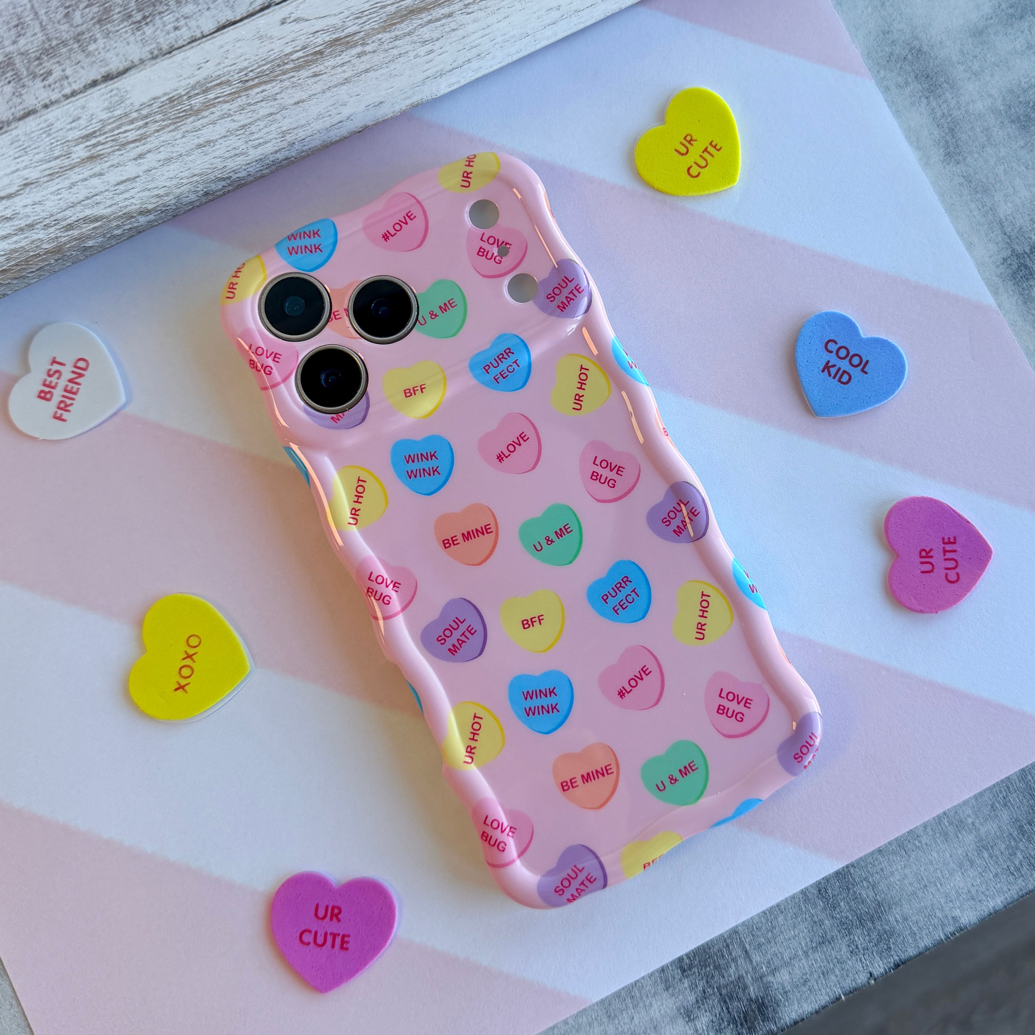 Pink wavy iPhone case featuring colorful candy conversation hearts with text like Be Mine, Ur Hot, and Soul Mate.