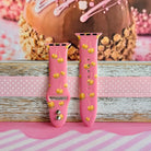 Caramel Coated Cutie Apple Watch band with both strap halves side by side on weathered wood and pink ribbon, showing the full caramel apple print.