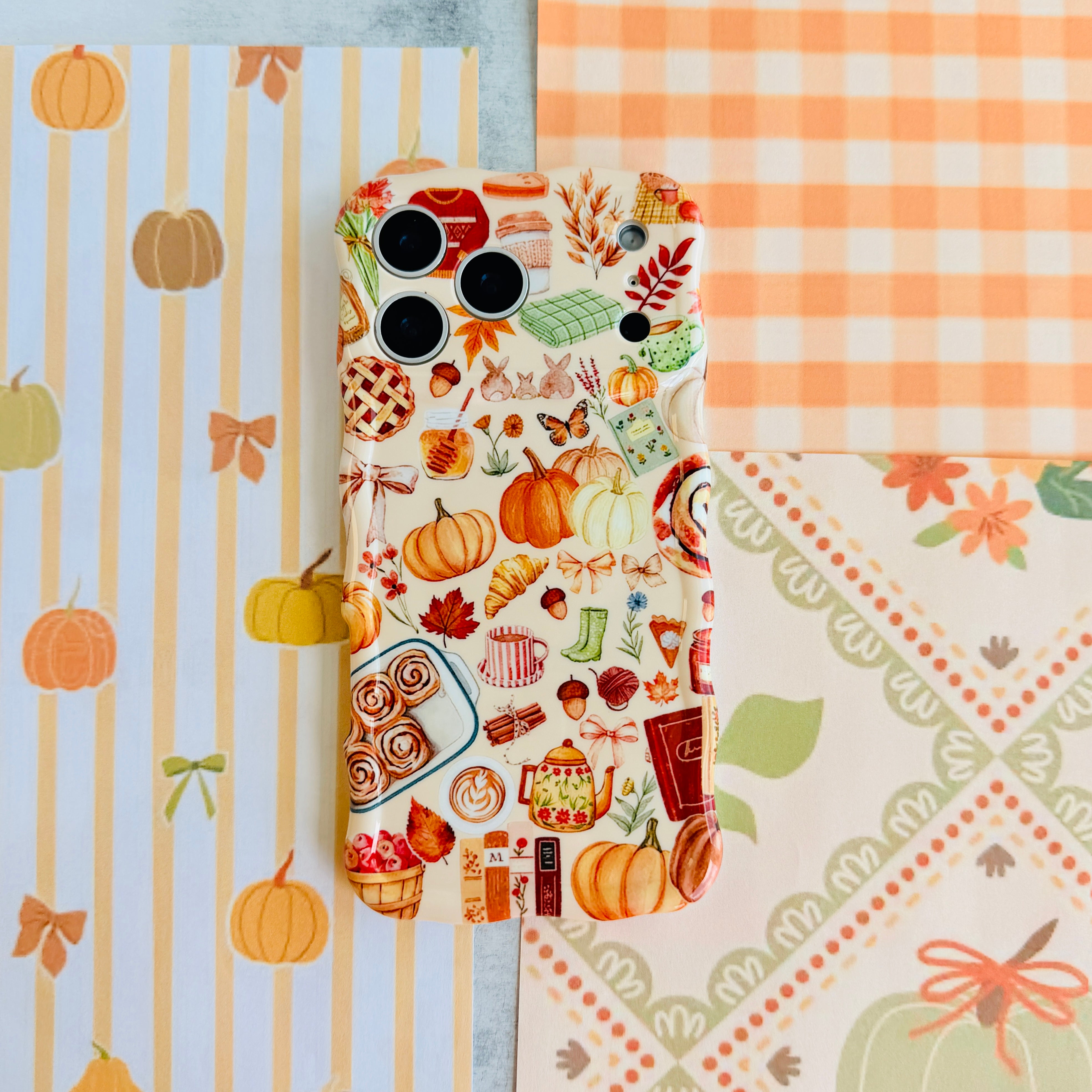 All The Fall Things Wavy Luxe MagSafe iPhone case flat lay on orange gingham and pumpkin-print paper, showing the full watercolor fall collage.