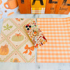 All The Fall Things Wavy Luxe iPhone case with the matching MagSafe grip ring attached, styled on a cream fall quilt print with an orange mug and wood sign.