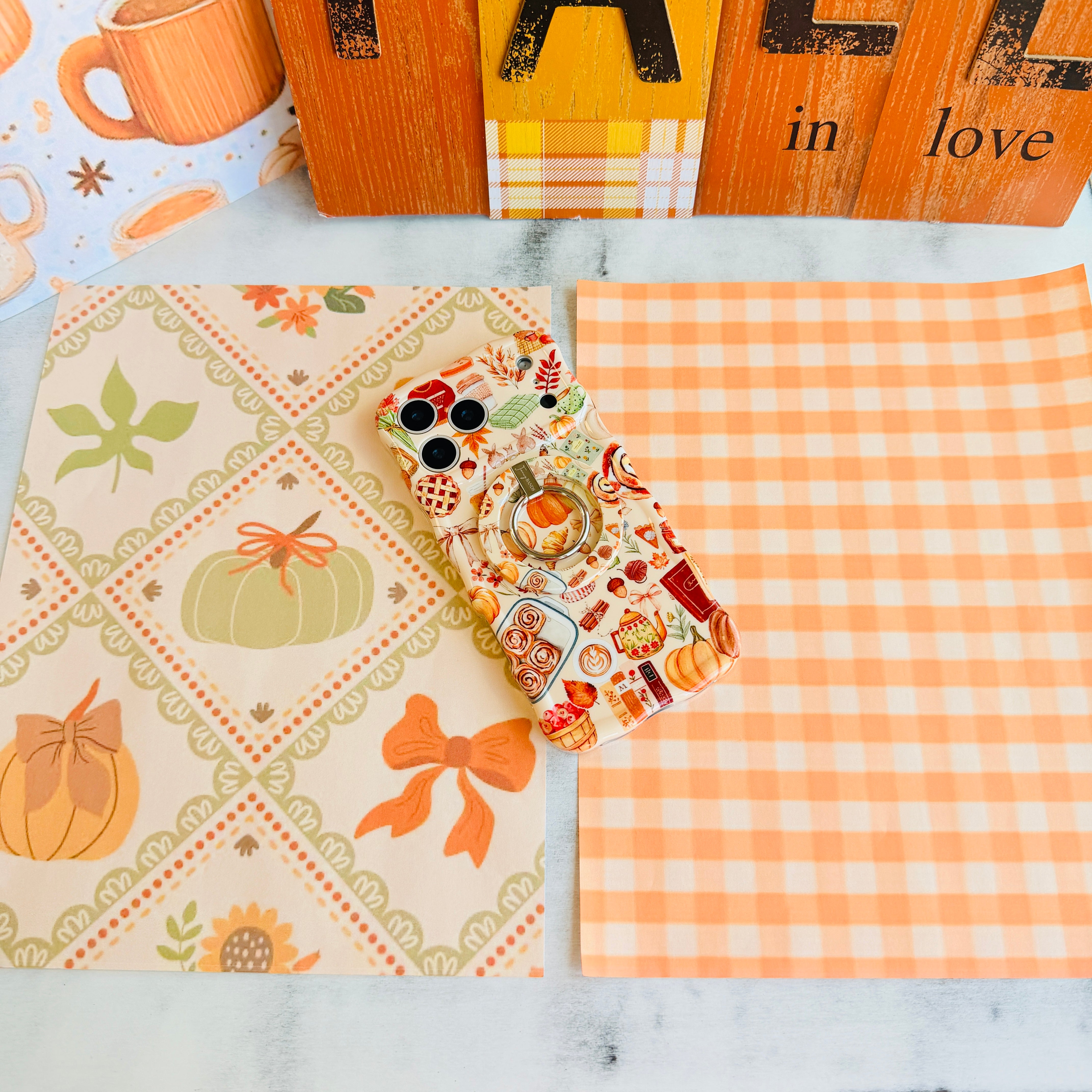 All The Fall Things Wavy Luxe iPhone case with the matching MagSafe grip ring attached, styled on a cream fall quilt print with an orange mug and wood sign.