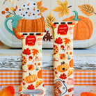 All The Fall Things Apple Watch band front view of both strap halves against a Spice and Cozy Nights fall sign, showing the cinnamon rolls, pumpkins and maple leaves in the print.
