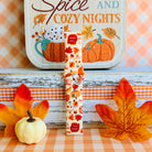 All The Fall Things Samsung Galaxy Watch band single strap half standing on weathered wood beside a white pumpkin, showing the watercolor collage print and quick-release end.