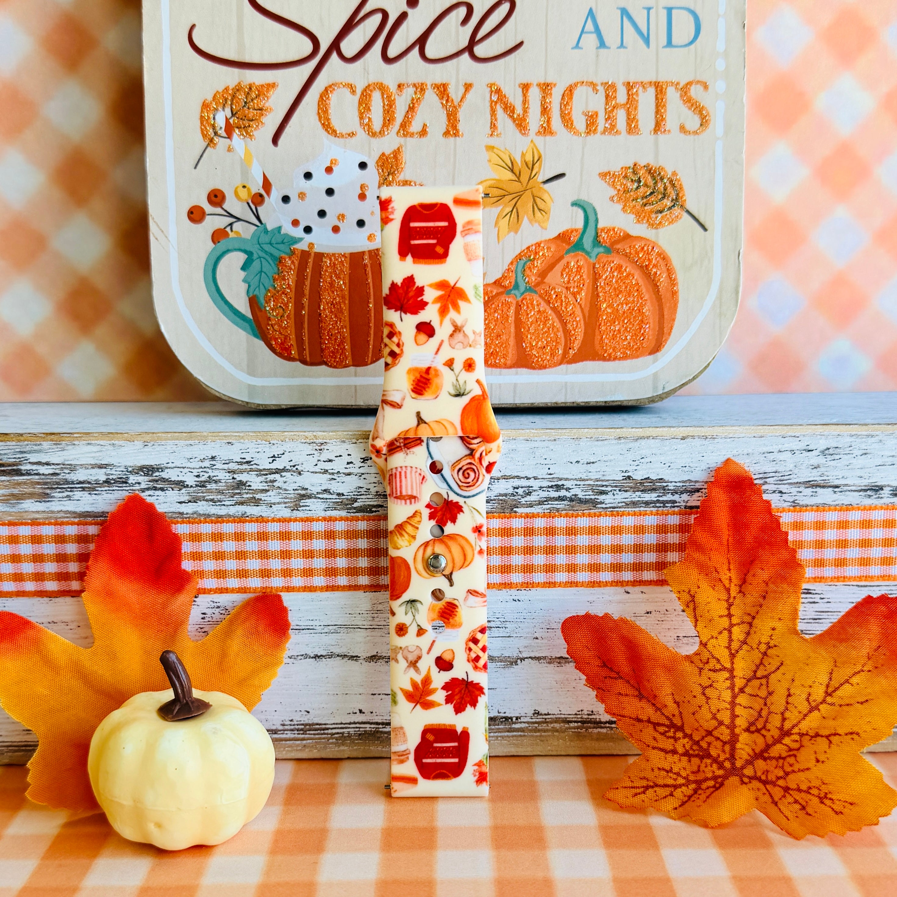 All The Fall Things Samsung Galaxy Watch band single strap half standing on weathered wood beside a white pumpkin, showing the watercolor collage print and quick-release end.