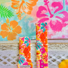 Sunset Hibiscus silicone Samsung Watch band with vibrant pink, orange, yellow, and teal tropical hibiscus floral print, shown displayed and worn on Apple Watch against a colorful tropical floral backdrop.