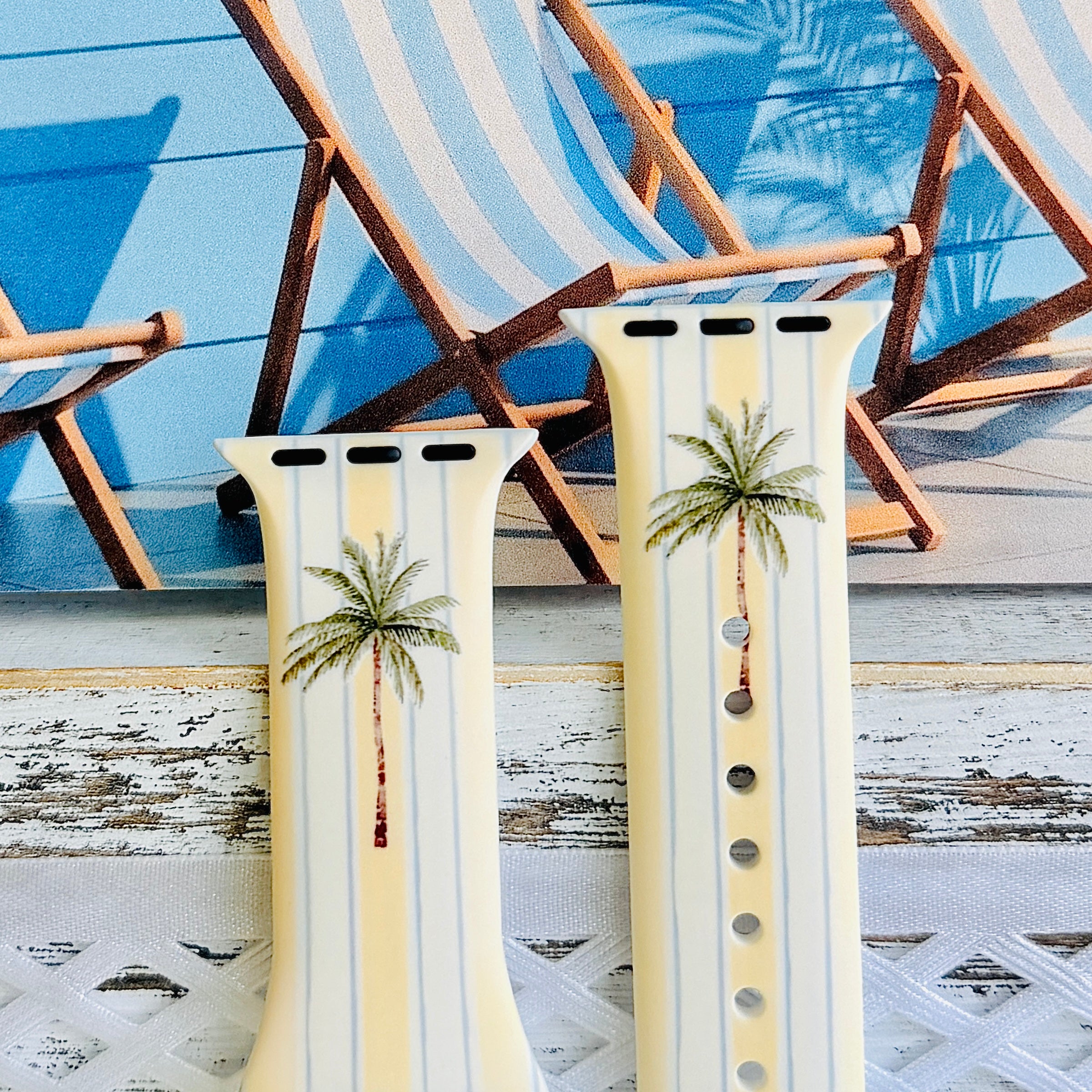Palm Shore Club silicone Apple Watch band with hand-painted palm trees over soft blue and yellow cabana stripes on an ivory base, shown displayed and worn on Apple Watch against a coastal beach club backdrop.